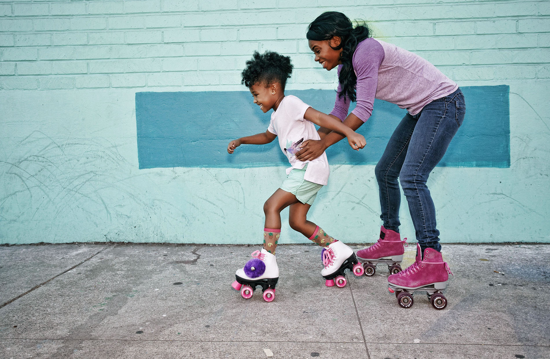 Black mother holding waist of daughter wearing roller skates