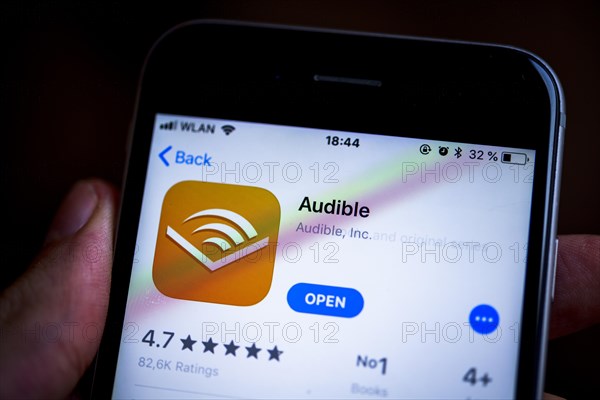 Hand holding an iPhone displaying the Audible app