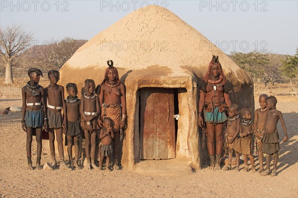 Himba women with children in front of a sleeping hut