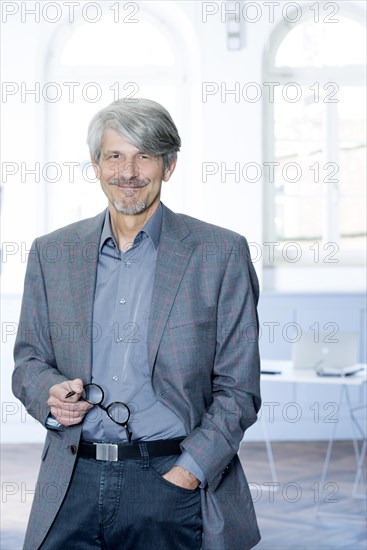 Man with glasses on his hand in front of the window of his office