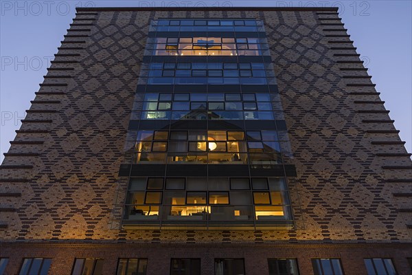 Clinker facade with illuminated rooms from the former egg cold store at dusk