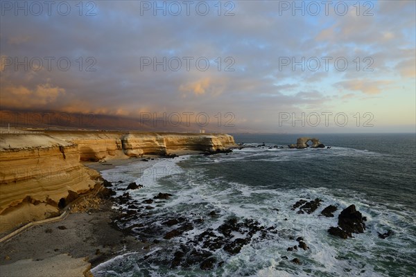 Rocky coast with arch La Portada at sunset with clouds