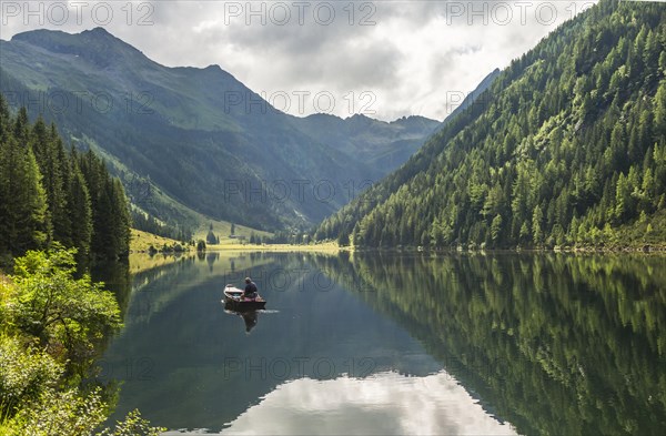 Fisherman on Lake Riesachsee with reflection of forest and mountains