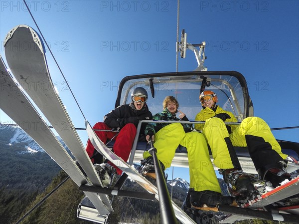 Three teenagers on chairlift with skis and snowboard