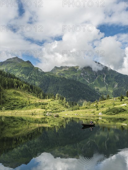 Fisherman on Lake Riesachsee with reflection of forest and mountains