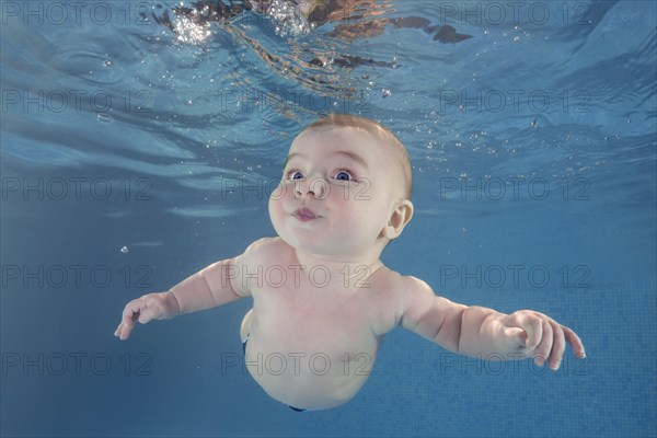 Little baby boy learning to swim underwater in a swimming pool