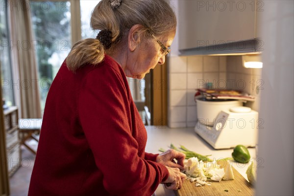 Senior cuts vegetables in the kitchen