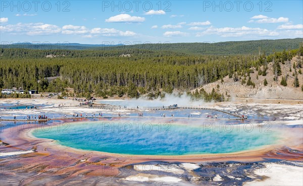 Visitors on footbridge over steaming hot spring with coloured mineral deposits