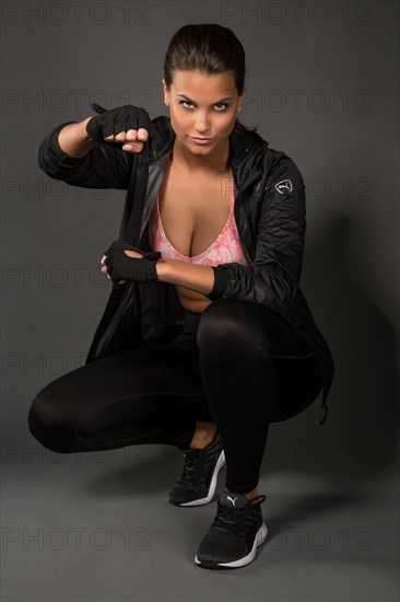 Young woman with dark hair tied together poses in a sporty outfit