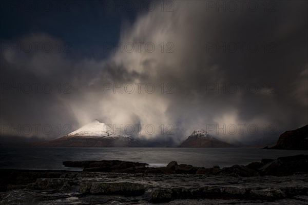 Big rocks in the water of the North Sea with snow-covered Cullin mountains in the background