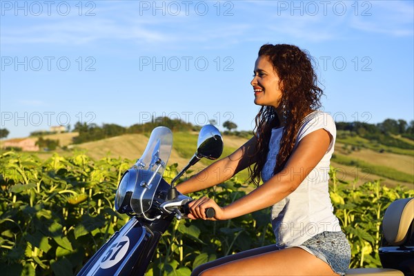 Woman on Vespa Primavera scooter in front of sunflower field