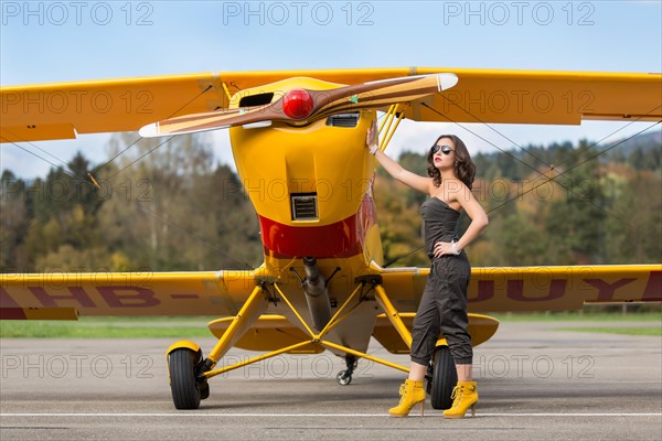 Young woman with sunglasses in overall and boots posing in front of double-decker airplane