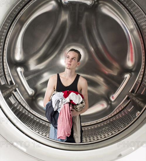 Conceptual image of a young confused man holding laundry inside a washing machine