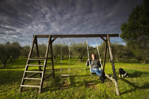 Girl swinging on a wooden swing in front of an olive grove