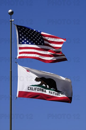 The US-American flag and the Californian flag flying on a flagpole against a blue sky