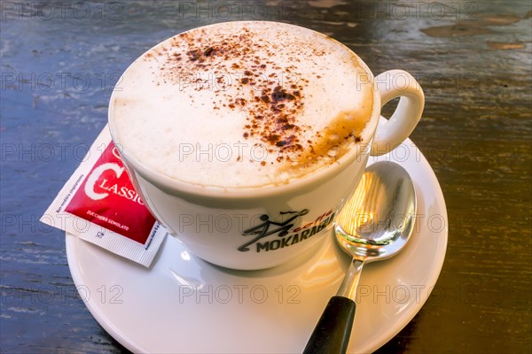 Cappuccino with a sugar sachet and a spoon