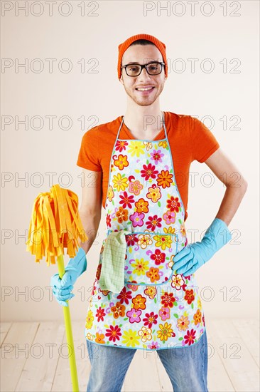 Young man wearing an apron and cleaning gloves holding a cleaning mop