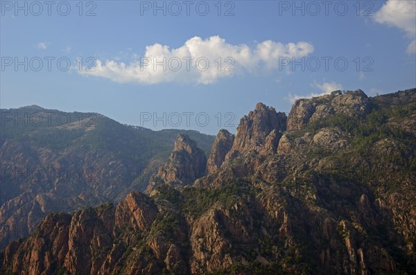 The typical rocky mountains of western Corsica near Evisa below a blue sky with a lone white cloud. Evisa illuminated by warm evening light surrounded by mountains. Evisa is in the department Corse-du-Sud