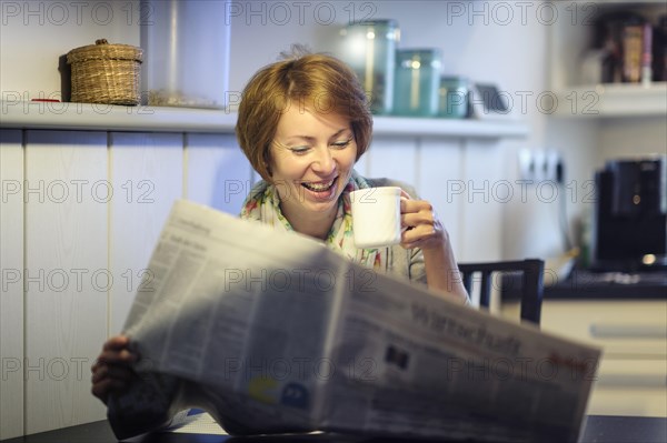 Woman sitting at the kitchen table reading the newspaper