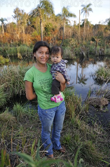 Young mother holding a child in her arms in front of a pond in the community of Mbya-Guarani Indians