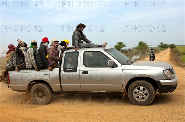 Small pickup truck carrying farm workers in the crowded cargo bay on a country road