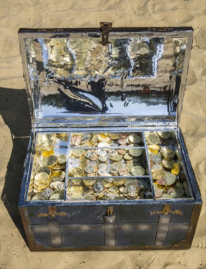 Treasure chest with gold and silver coins on the sand