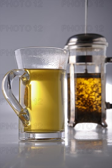 Tea glass in front of a teapot with herbal tea