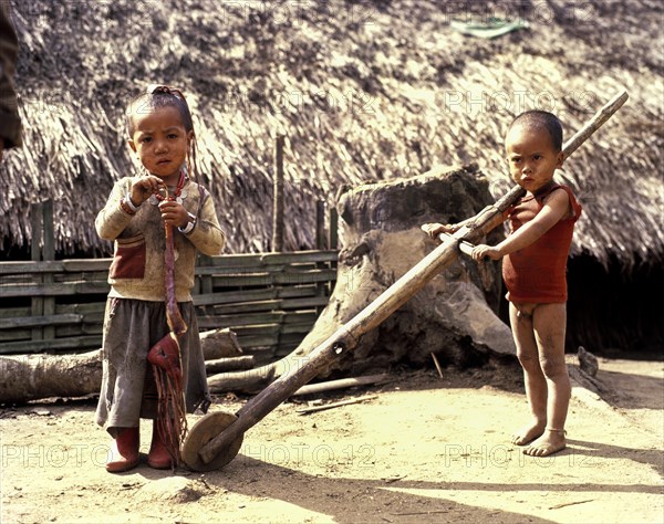 Akha boy and Akha girl in torn clothes with primitive toys