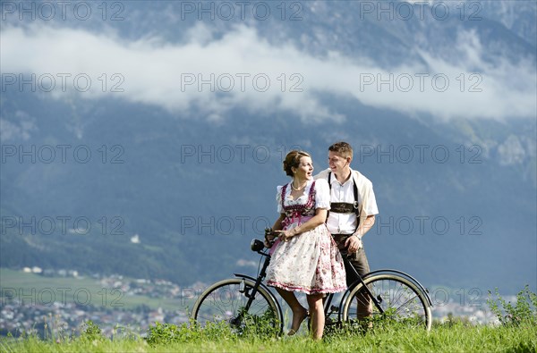 Man and a woman wearing traditional costume with an old bicycle within a natural landscape