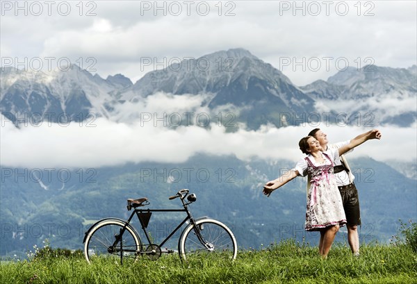 Man and a woman wearing traditional costume with an old bicycle within a natural landscape