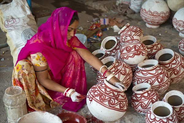 Indian woman wearing a headscarf sitting on the floor and painted clay water jars with traditional ornamentations