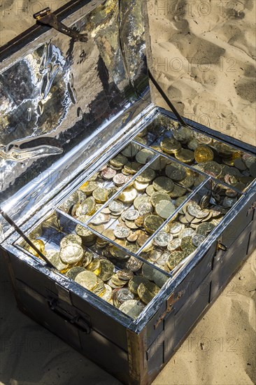 Treasure chest with gold and silver coins on the sand