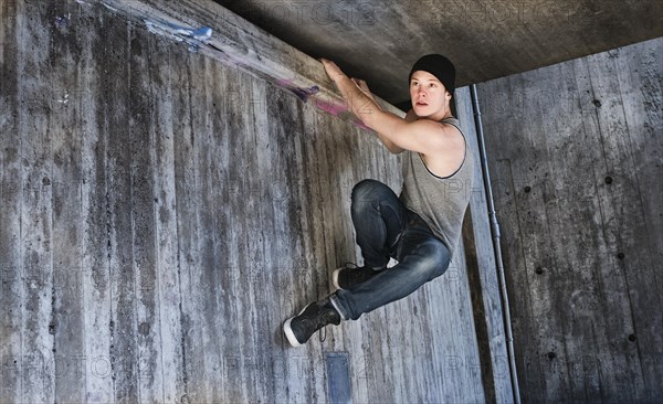 Young man hanging in a parkour move on concrete wall