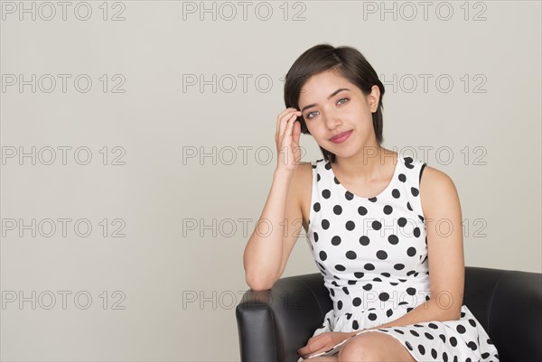 Young woman wearing a dotted dress sitting in leather armchair