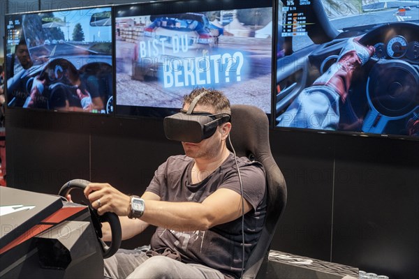 Visitor wears Virtual Reality glasses in a driving simulator for car racing at gamescom