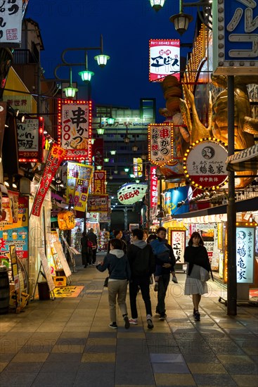 Many colorful neon signs in a pedestrian zone with shops and restaurants