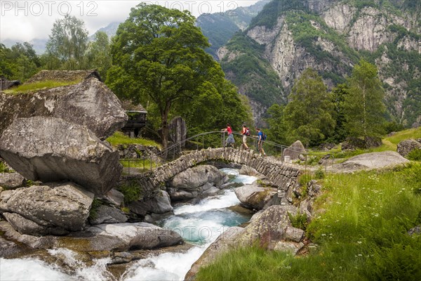 Three hikers crossing a medieval arch bridge