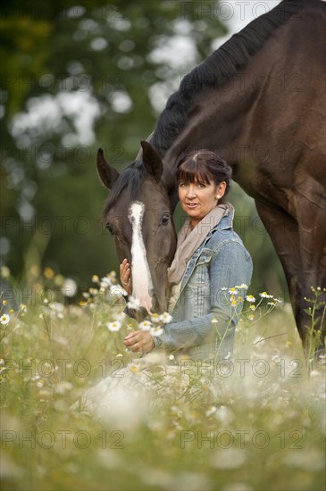 Woman standing beside a Hanoverian horse in a meadow