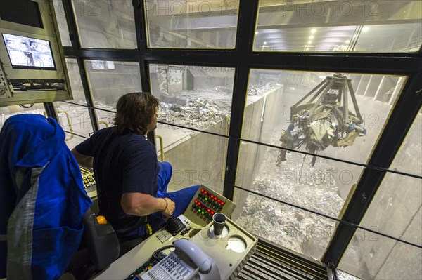 A crane operator is supervising the transport of waste to the incinerators in a waste incineration plant