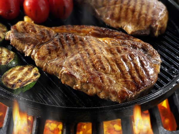 Sirloin beef steaks and tomatoes being pan fried on a BBQ