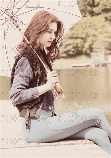 Young woman sitting on a jetty holding a white parasol