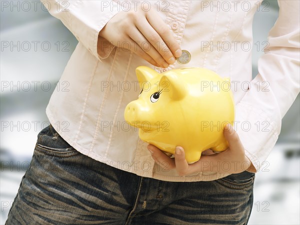 Girl putting euro coin into in piggy bank