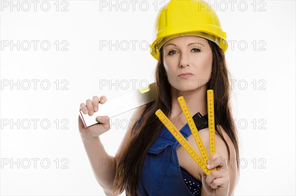 Woman wearing blue overalls and a hardhat holding a folding carpenter's ruler and a spirit level