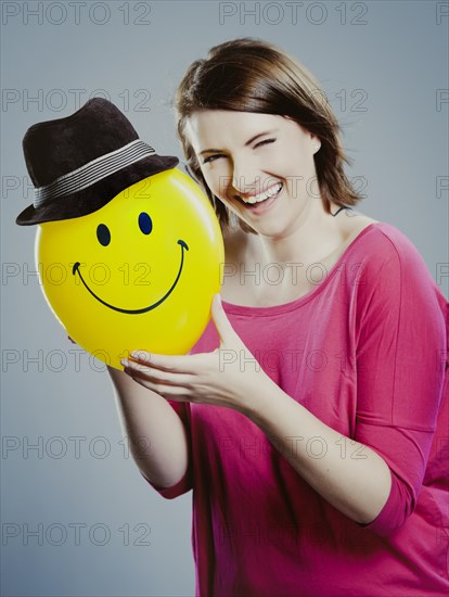 Smiling young woman holding a smiley face balloon