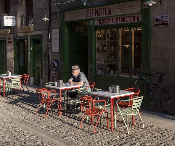 Old man reads newspapers and drinks coffee at a cafe table in early morning