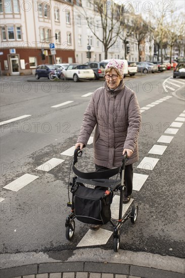 Senior citizen with rollator crosses a street in the city