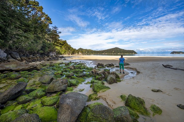 Young woman standing on beach with moss-covered rocks