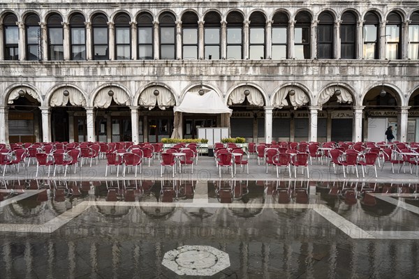 Red garden chairs in front of a coffee house near Acqua alta on St. Mark's Square