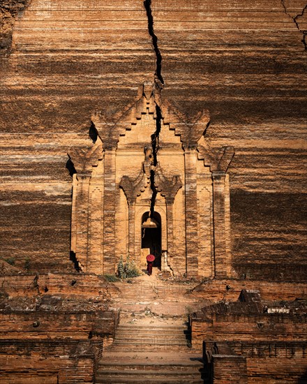 Buddhist monk stands with red umbrella in the entrance of Mingun Pagoda