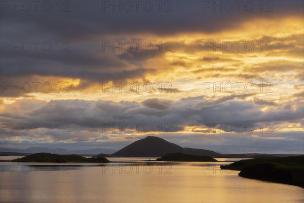 Hills with clouds in the evening light are reflected in the lake Myvattn